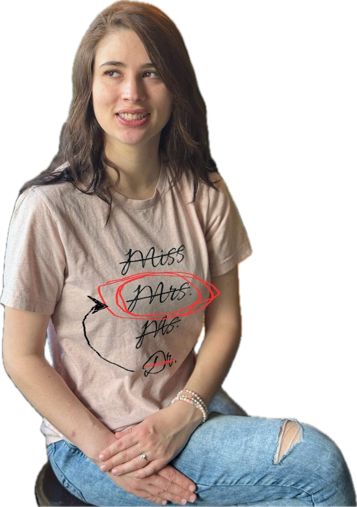Caeli wearing her Miss, Mrs., Ms., Dr. shirt where everything but Dr. is crossed out. But someone crossed out the doctor part too and drew an arrow back to Mrs. and circled it.