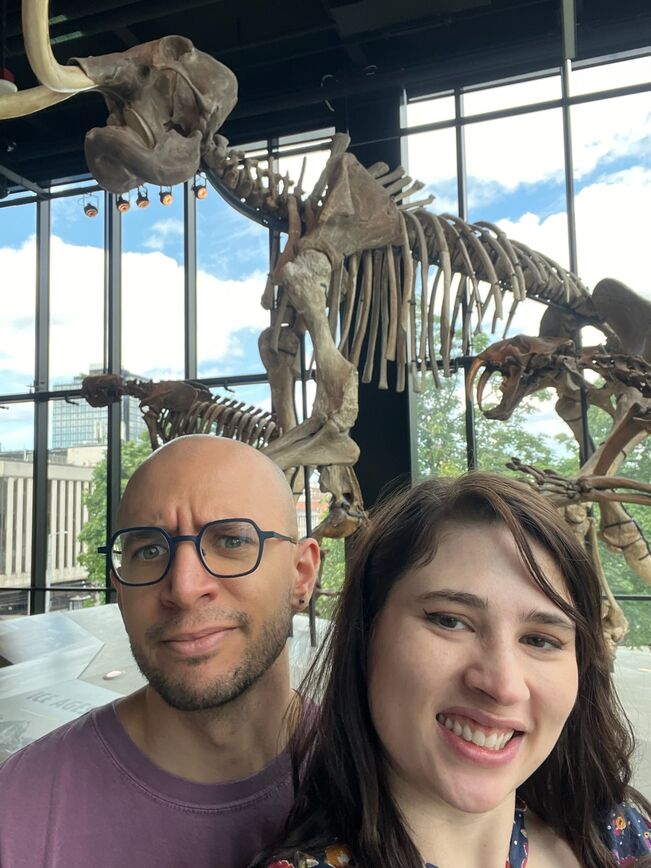 Caeli and Jared standing in front of a prehistoric animal skeleton exhibit